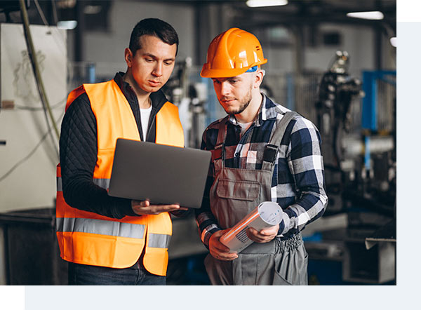 Dois operários conversando em uma fábrica com olhando para um notebook que está na mão de um deles.