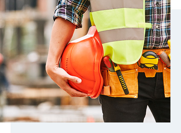 Close da cintura de um operário com um cinto de ferramentas e um capacete laranja na mão direita